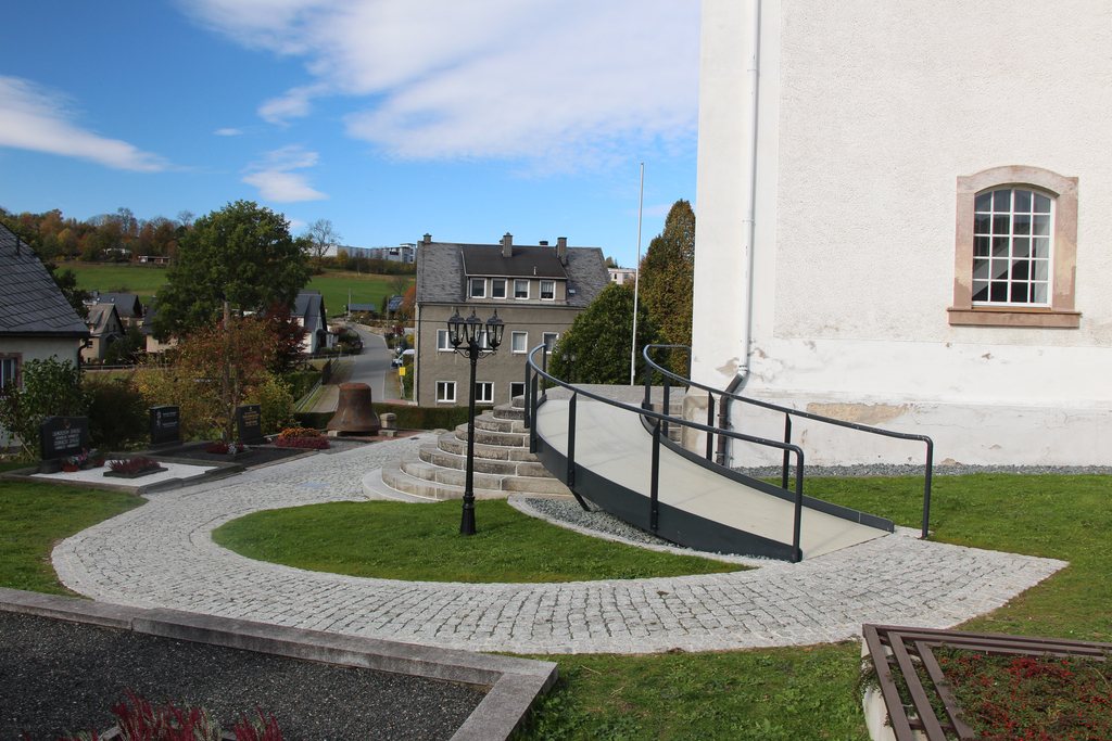 Geschwungene barrierefreie Rampe führt zu einem Kircheneingang mit Steinmauer